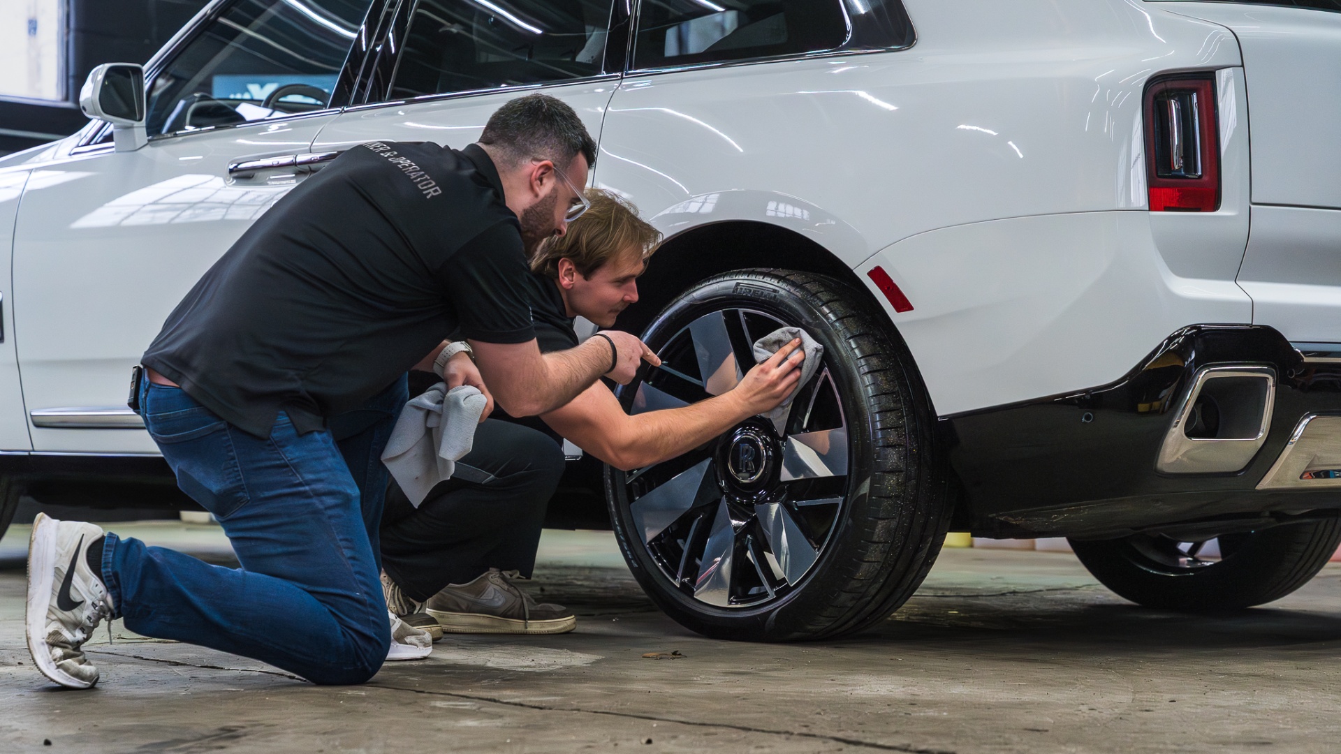 Two technicians ceramic coating a Rolls-Royce Cullinan wheel